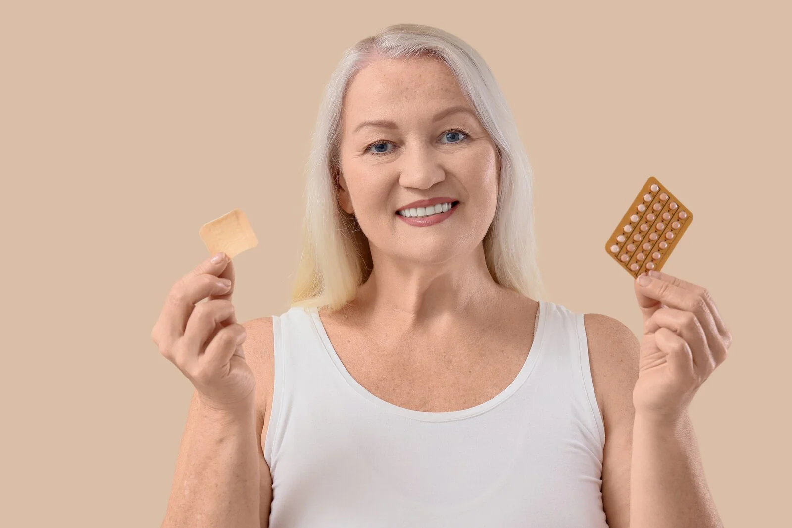 A woman holding a transdermal patch in one hand and a blister pack of tablets in the other